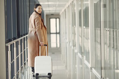 Stylish woman walking through a modern airport terminal with a white suitcase, ready for luxury travel.