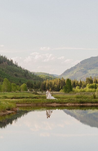 Stunning mountain wedding portrait with the bride and groom reflecting on the lake at Camp Hale in Vail, Colorado