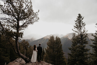 Bride and groom standing on a hill looking out at the mountains, captured by Kelsey Vera Photography, intimate and romantic wedding photographer in Airdrie, Alberta. Featured on the Bronte Bride Vendor Guide.