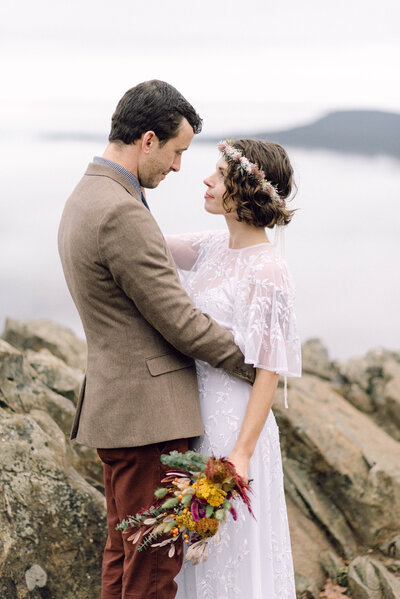 Cinematic wide shot of the couple embracing on the summit, with soft focus and natural light.
