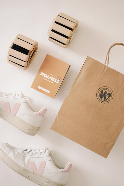 Flatlay of The Wellness Passport collateral, bag, ankle weights, and Veja shoes