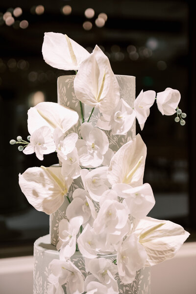 Pale sage green tiered wedding cake with white leaf stencil background and cascading white sugar flower anthuriums