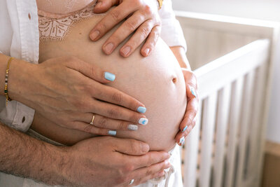 Een pure en liefdevolle foto zwangere buik met handen van de ouders tijdens een zwangerschapsshoot binnen - Irene Maris Fotografie
