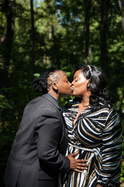 A newlywed couple kissing while standing in a wooded area 