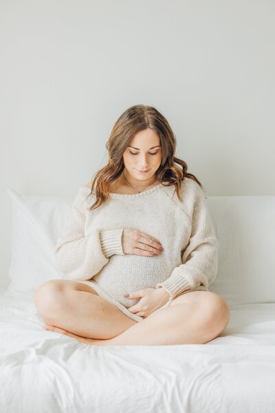 pregnant woman sitting on bed holding belly
