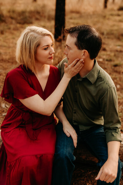 Couples photography in Cleveland TX - woman in red dress sitting on partner's lap, forehead kiss outdoors