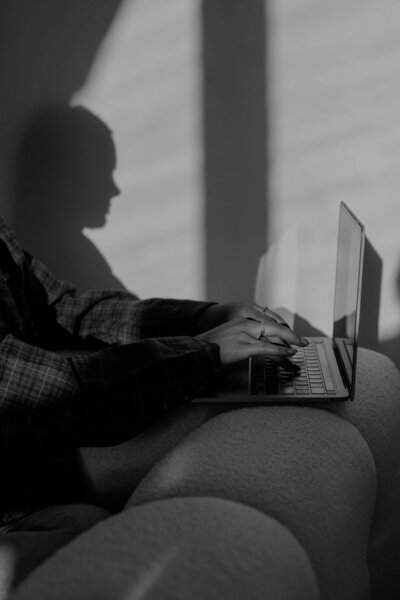 Woman sitting on couch typing on laptop - Refined Web Design