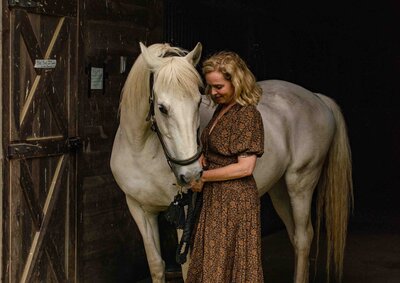 Woman gently resting beside her white horse in a peaceful Berkshire field before an equine-assisted session