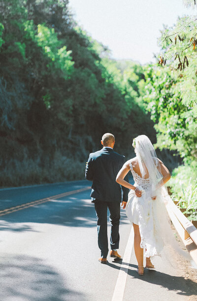 bride and groom walk along the road casually wearing their suit and dress. Playful wedding photo