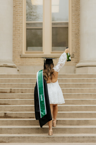 A Colorado State University graduate celebrates with a bottle of champagne at The Oval in Fort Collins.