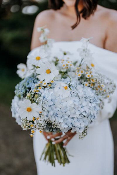 Bride holding wedding bouquet of blue hydrangea, cosmos, camomile flowers