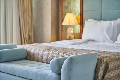 A cozy, inviting hotel suite with a soft blue bench at the foot of a beautifully made bed, warm lighting, and timeless details that make you feel right at home.