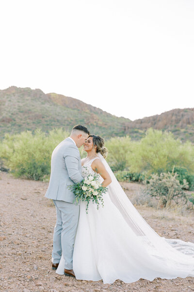 Elegant embrace at Superstition Manor: Groom sidewise, bride with a graceful tilt, holding bouquet, capturing timeless romance in stunning photography