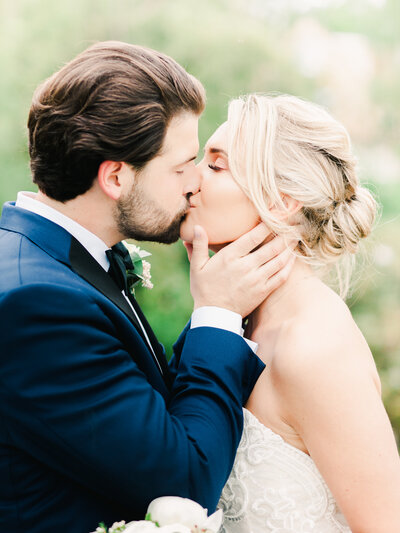 Groom wearing black tie suit kisses his bride at the ceremony