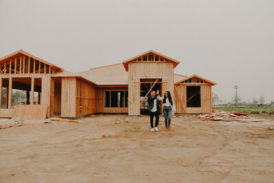 Bakersfield realtor couple walking in front of new construction home framing for sale