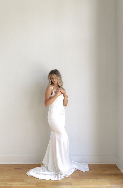 Bride in a sleek satin gown posing against a plain wall.