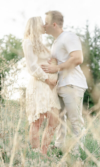 Blurred photo of a man kissing his pregnant wife at their outdoor maternity photo session with Kristie Lloyd.
