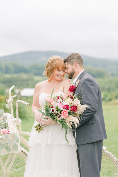 bride and groom in the mountains with antique bike and beautiful red, pink and blush bouquet