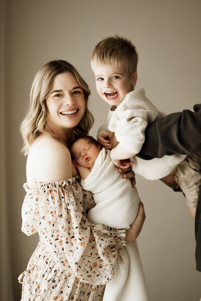 Mum holding sleeping baby with toddler happy and smiling in Studio