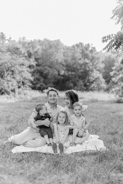 A black and white photo of a family of five sitting on a blanket during an outdoor photo session with Boston family photographer Corinne Isabelle