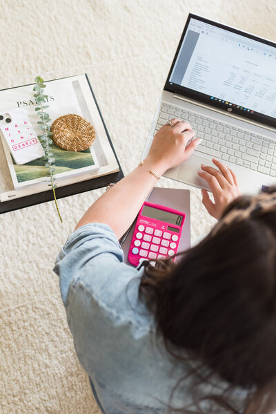 Woman using a pink calculator and a laptop
