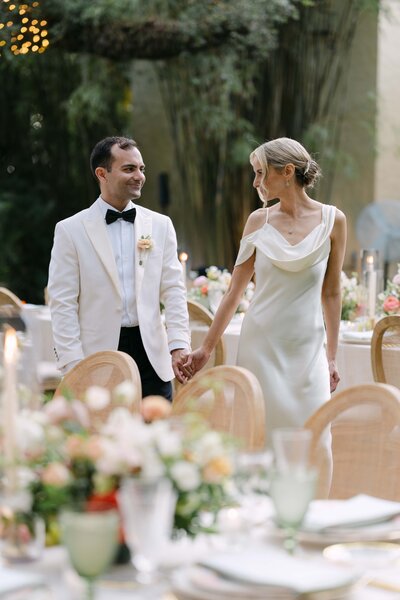 couple on their wedding gowns walinkg away from the camera, whiloe the bride looks back at it