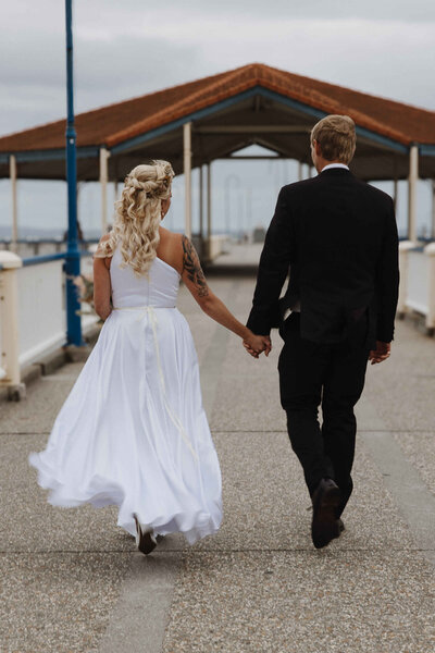 Sunshine Coast wedding couple walking hand-in-hand down a pier after their ceremony.
