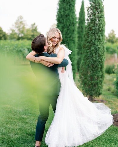 outdoor image by bauer creative of groom holding up bride joyously near cypress trees in minneapolis minnesota