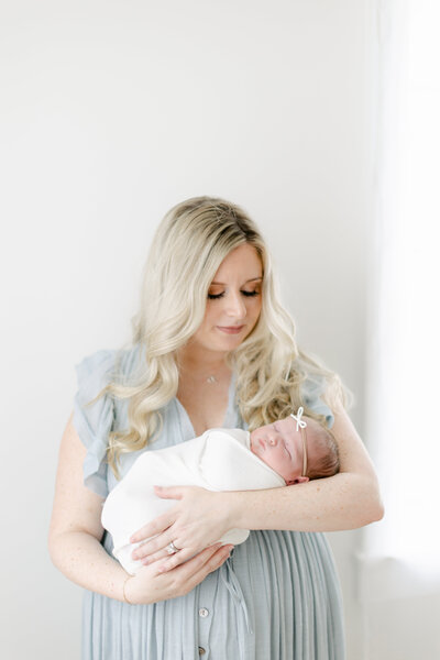 Infant swaddled in a white blanket wearing a bow photographed by South Jersey Baby Photographer Tara Federico