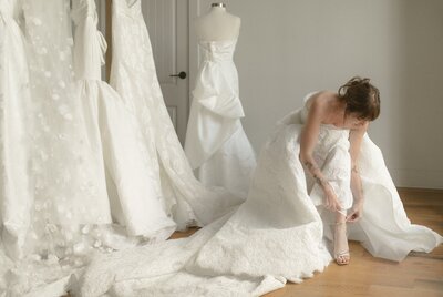 Bride adjusting her lace gown while standing in a bridal studio.