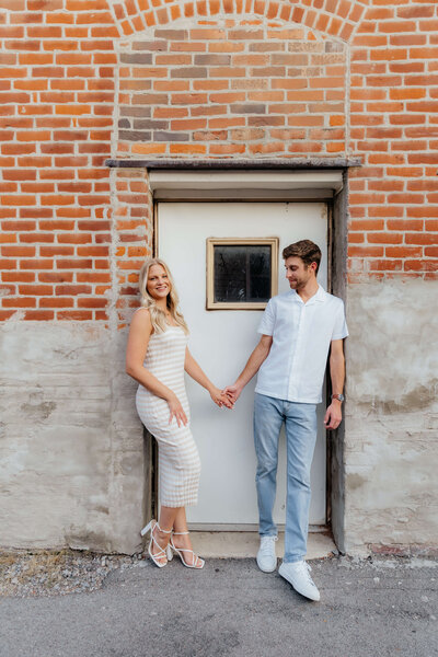 Modern Ohio couple holding hands by rustic brick wall, casual and candid engagement photography for laid-back Midwest lovers