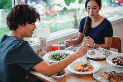 Two people sitting at a table eating pasta, pizza and a salad