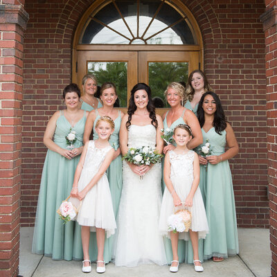 bride standing in front of building with bridesmaids and flower girls