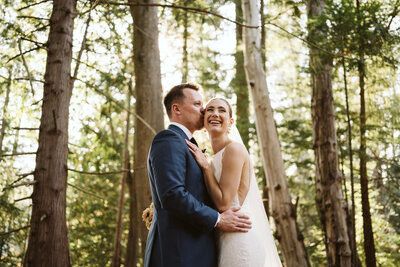 A couple posing for their wedding photos in front of the forest at Camp Fircom on Gambier Island.