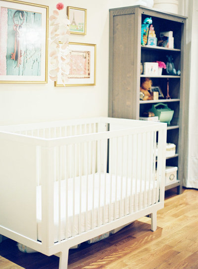 A nursery with a white crib, three wall hangings, and decorated bookcase.