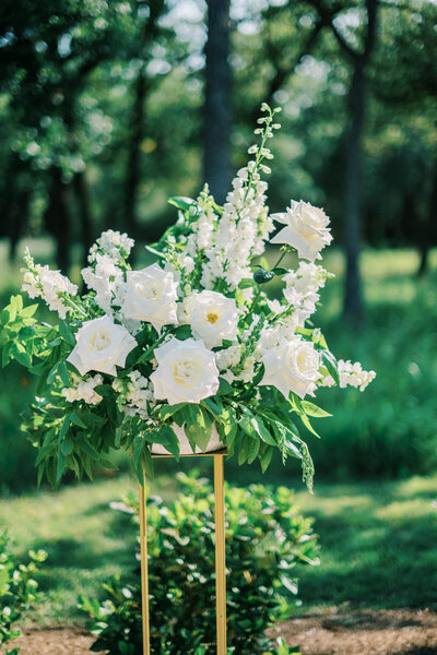 White floral arrangement and greenery on a gold stand