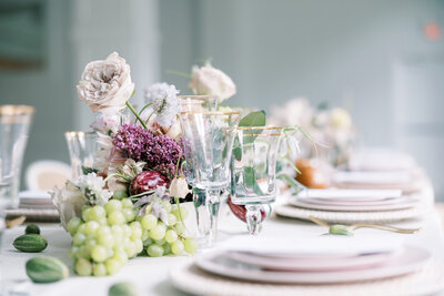 Close-up of an elegant reception table featuring pastel florals, green grapes, and gold-rimmed crystal glassware in a bright Houston venue.