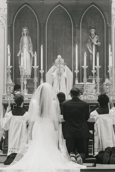 Catholic priest holding the Eucharist above a kneeling couple during the wedding Mass