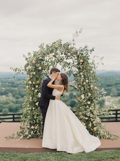 Bride and Groom kiss in front of organic floral arch at Trinity View Farms in Nashville Tennessee photographed by Nashville luxury wedding photographer Magnolia Tree Photo Company