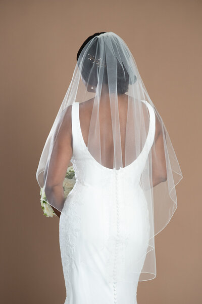 Bride wearing a fingertip length serged edge veil and holding a white and black bouquet