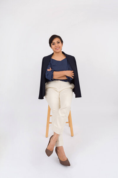 Studio photograph of a professional woman leaning on a stool with a blazer draped over her shoulders