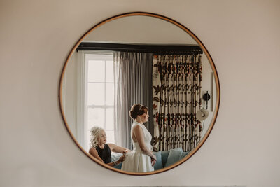 A mirror showing someone helping zip up a wedding dress