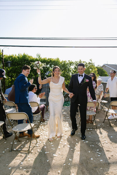 Katie and Sebastian exiting their ceremony while the guests throw white rose petals.
