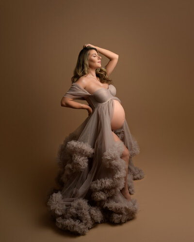 Textured studio maternity gown in taupe with tulle skirt and fitted bodice – dramatic lighting setup