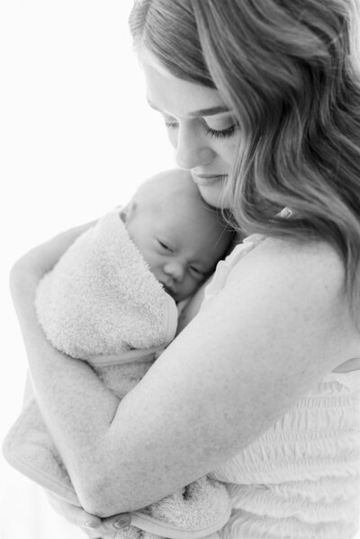 Black and white portrait of a mother gently holding her wrapped newborn during a studio session with a Kansas City newborn photographer.