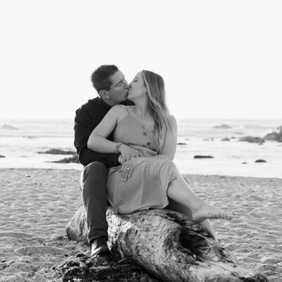 Fiance kissing on log on beach engagement photos