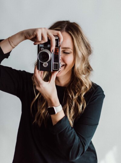 Photographer woman holding a vintage camera laughing behind it