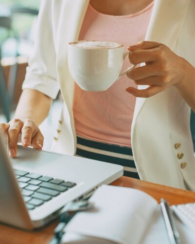 WOMAN TYPING ON LAPTOP WITH COFFEE