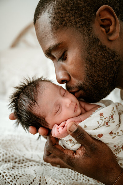 Father leans down to kiss his newborn baby who is sound asleep. 