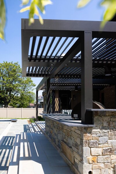 Black StruXure pergola cantilevered over a stone bar and outdoor kitchen. 